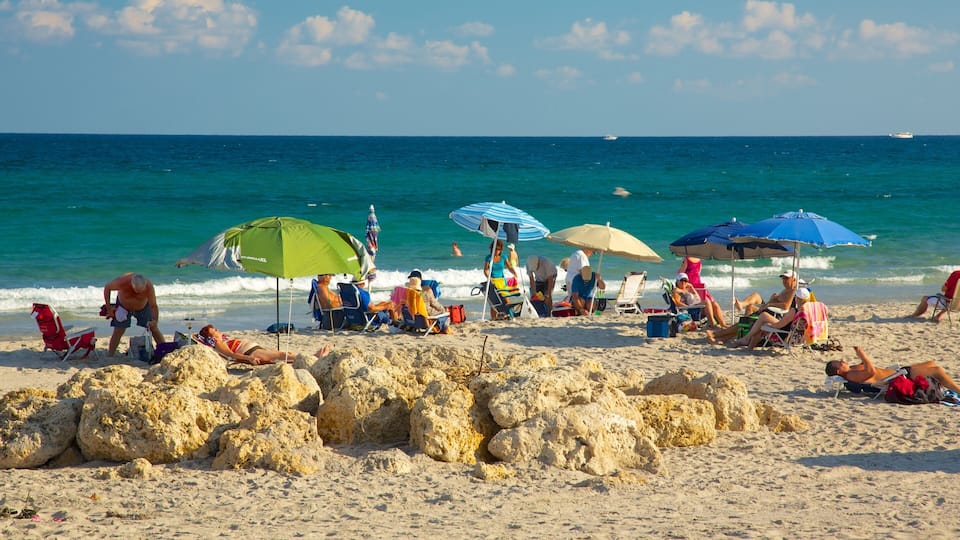 A beach with people relaxing under umbrellas, a rocky shoreline, and a boat in the distance.
