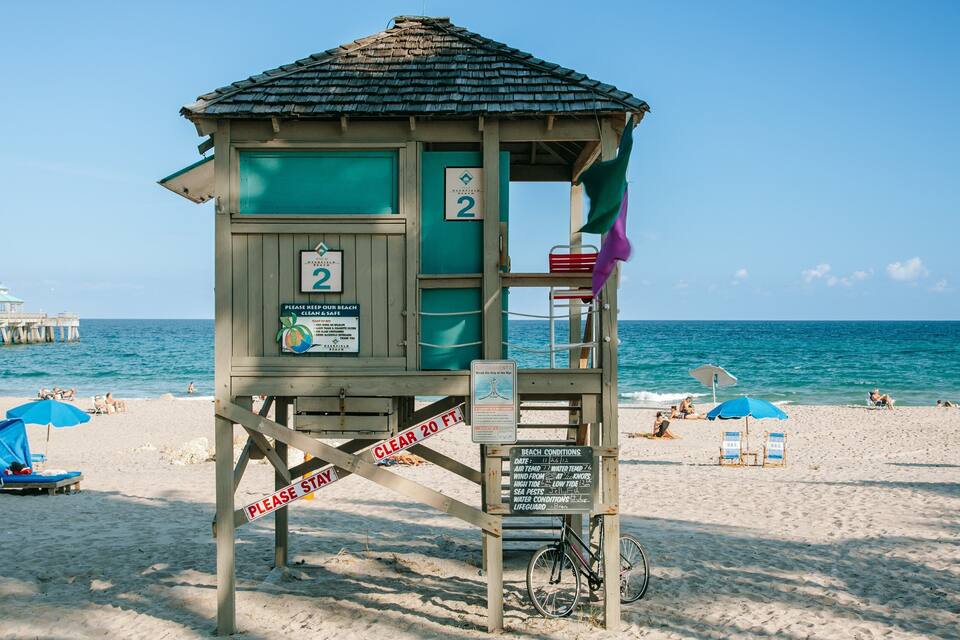 Torre de salvavidas con un cartel que indica una distancia despejada de 6 metros. Se ven sombrillas y gente en la arena.