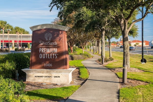 Schild von SilverSands Premium Outlets, mit einem von Bäumen gesäumten Weg und einer Straße im Hintergrund.