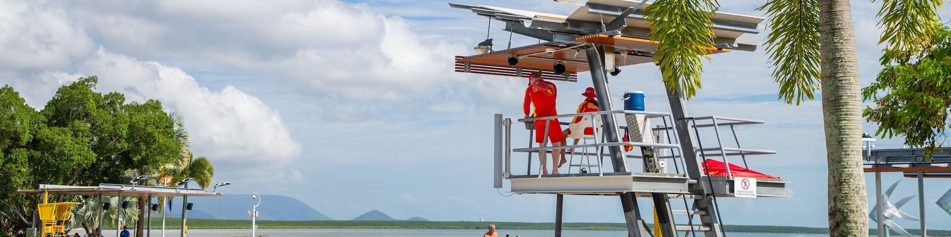 A beach with a lifeguard tower, palm trees, and a swimming pool.