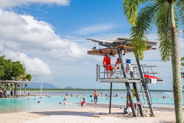 A beach with a lifeguard tower, palm trees, and a swimming pool.