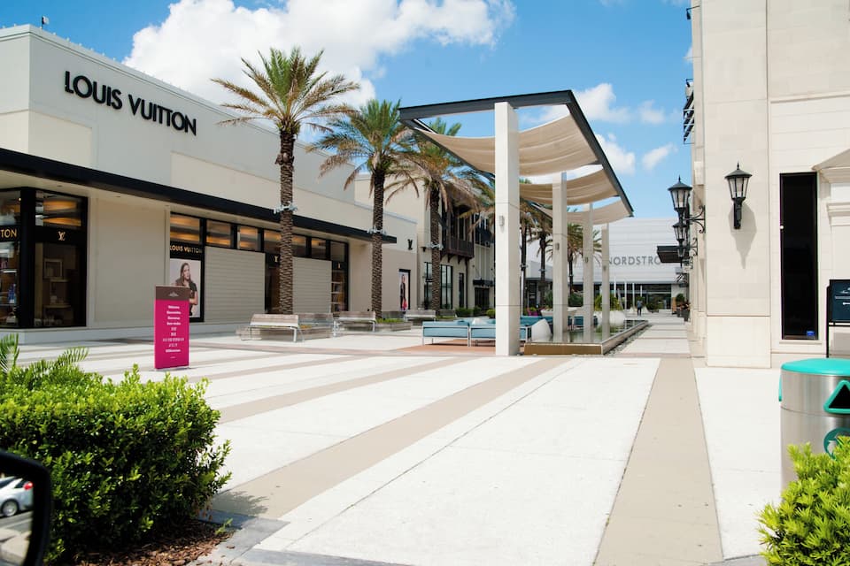 Uma loja Louis Vuitton, palmeiras e uma loja Nordstrom numa área comercial.