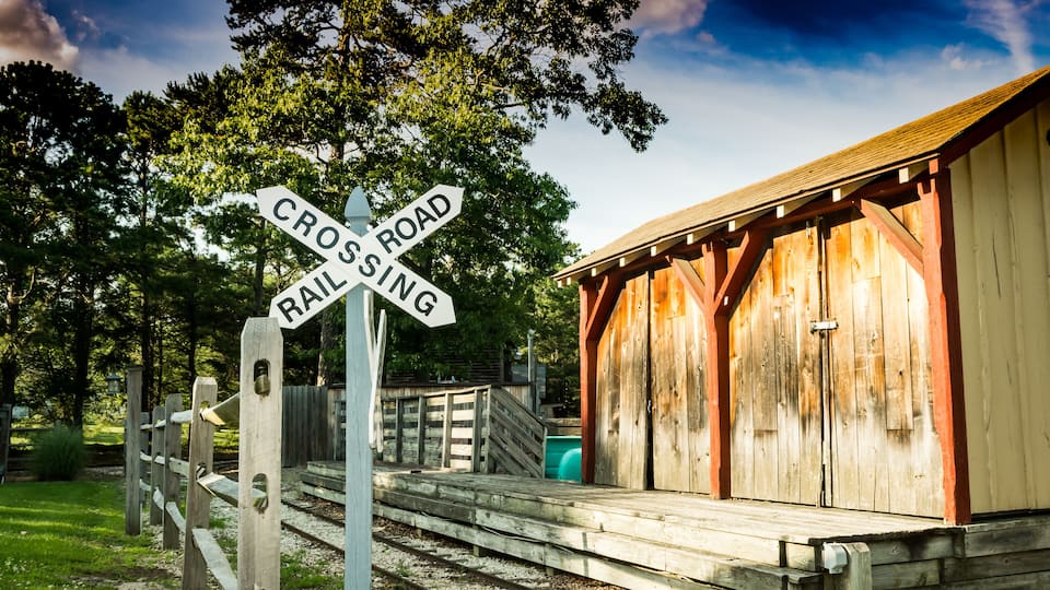 A wooden train station with a 'Crossing Road' sign and a 'Rail Sing' sign.