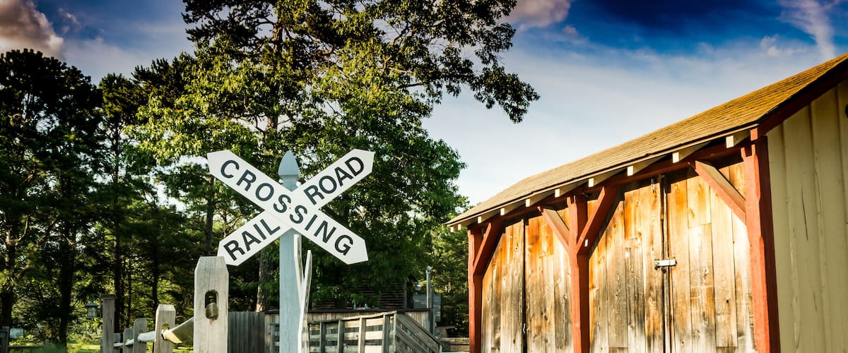 A wooden train station with a 'Crossing Road' sign and a 'Rail Sing' sign.