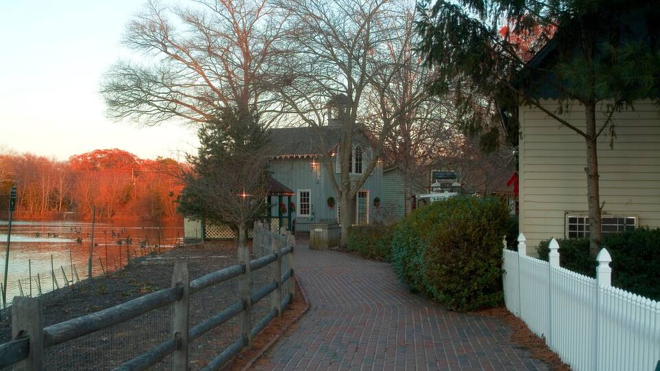 A brick pathway leading to a house with a white fence and trees.
