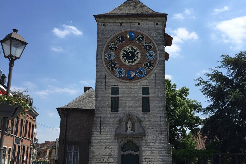 A historic stone tower with a large circular clock and a statue at its base.