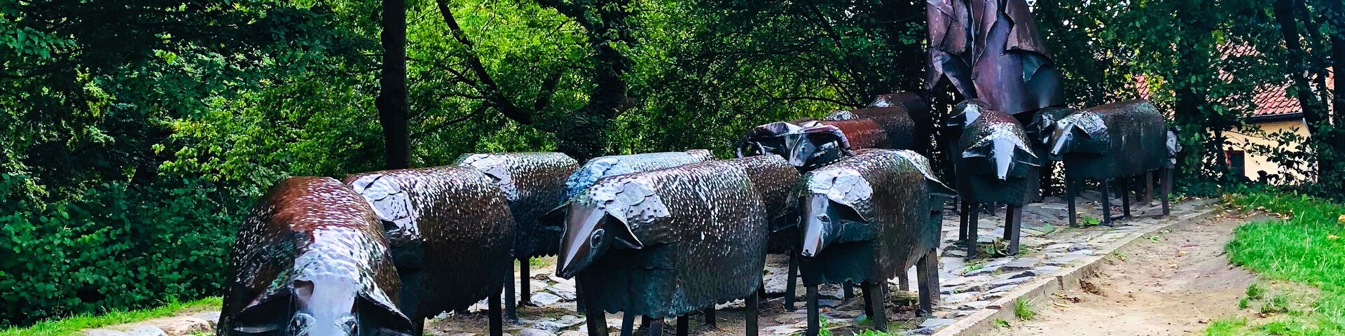 Un sendero adoquinado bordeado por esculturas de ovejas metálicas en un parque.