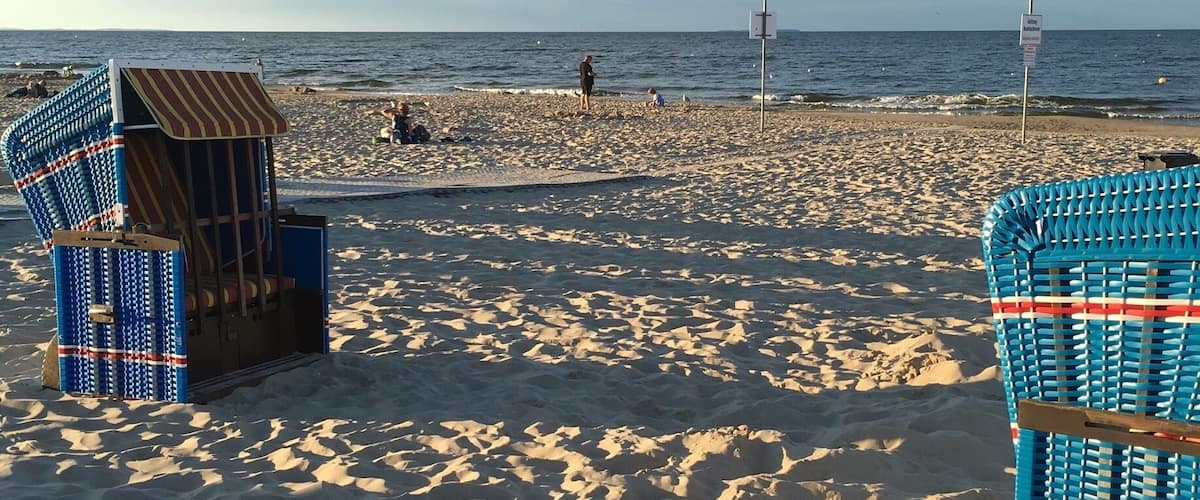 Una playa arenosa con dos sillas de playa azules y un paraguas de playa a rayas.