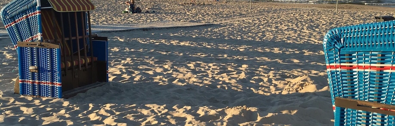 Uma praia arenosa com duas cadeiras azuis e um guarda-sol listrado.