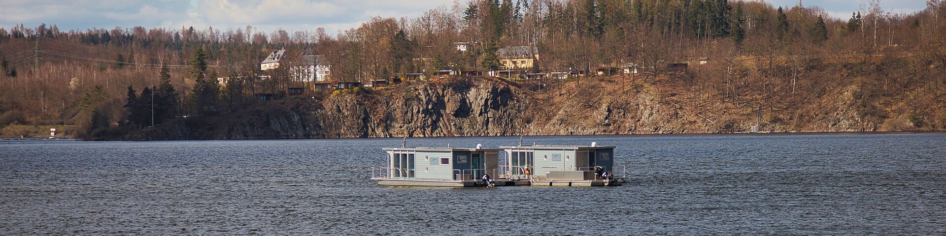 Um lago com duas casas flutuantes e uma encosta arborizada ao fundo.