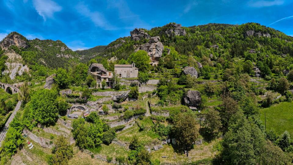 A mountainous landscape with a stone bridge, a small building, and lush greenery.