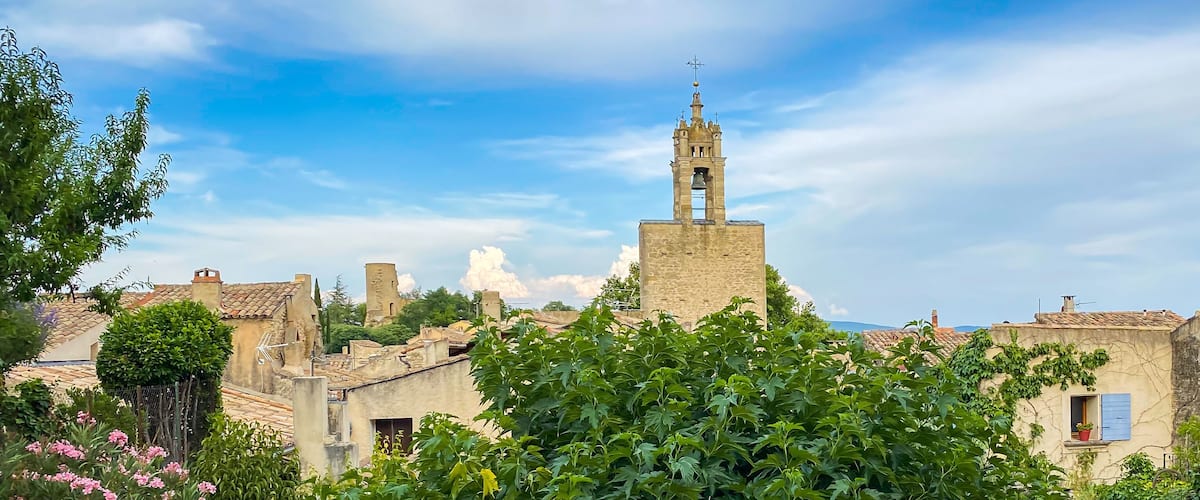 A historic town with a prominent bell tower, cobblestone streets, and lush greenery.