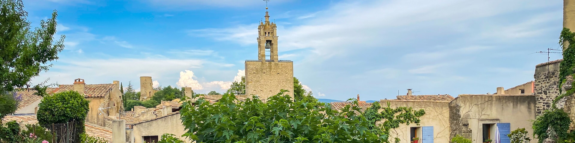 A historic town with a prominent bell tower, cobblestone streets, and lush greenery.