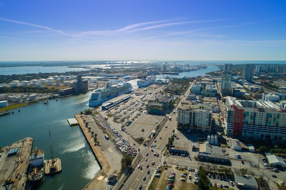 Un paisaje urbano costero con un gran crucero amarrado, un puente y edificios industriales.