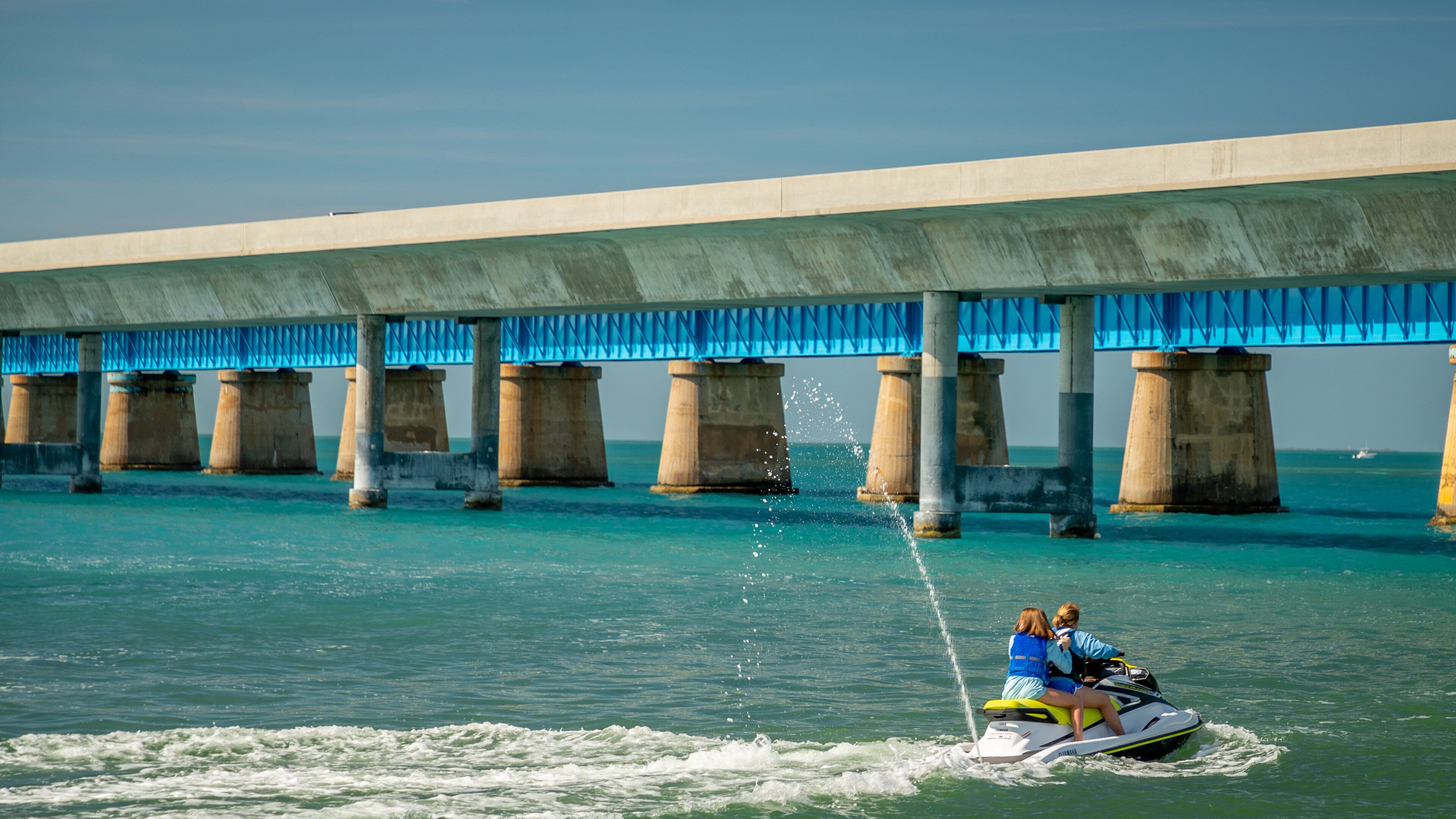 A bridge with blue railings and concrete pillars over turquoise water.