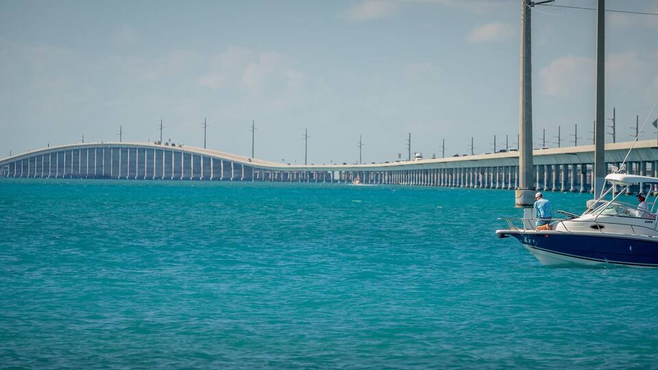 A coastal scene with a bridge extending into the water, a boat docked near the shore, and a clear sky.