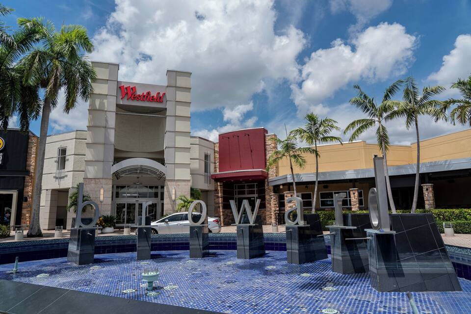 Um shopping Westfield com palmeiras e área de piscina com azulejos azuis.