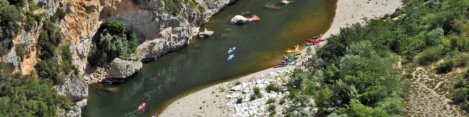 Un río con varias kayaks y un acantilado rocoso.