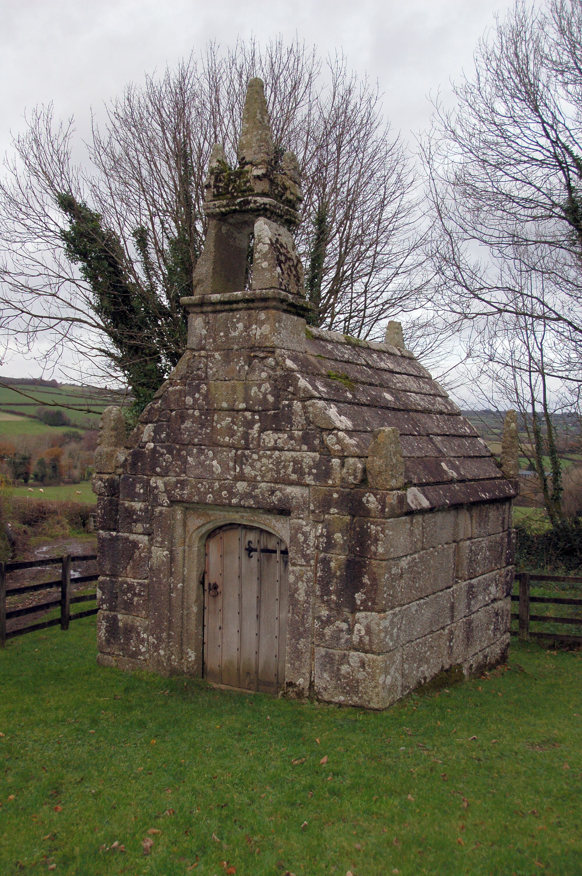 A small stone structure with a wooden door, surrounded by grass and trees.