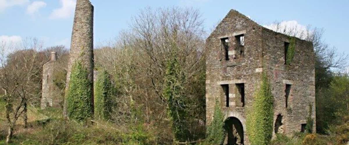 Holmbush Mine This is the remains of the buildings surrounding part of Holmbush Mine. Conservation work was carried out in 2007 and it is reasonably safe to walk around these buildings provided you are careful. There are the remains of three engine houses along with the boiler house chimney which is still just about standing. I have no specific information about the engine houses but the one in the foreground has a very wide arched entrance and if you walk inside you can still see the bolt holes which were used to anchor the engine to the ground. This building must have housed very large engine, possibly 100 inch cylinder. Such large engine were almost always used to pump water from the mine workings.