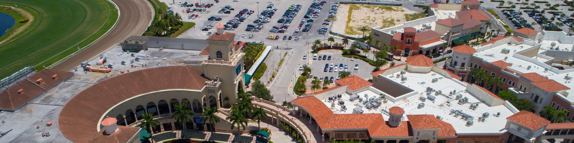 An aerial view of a racetrack, parking lots, and a central plaza with buildings and palm trees.