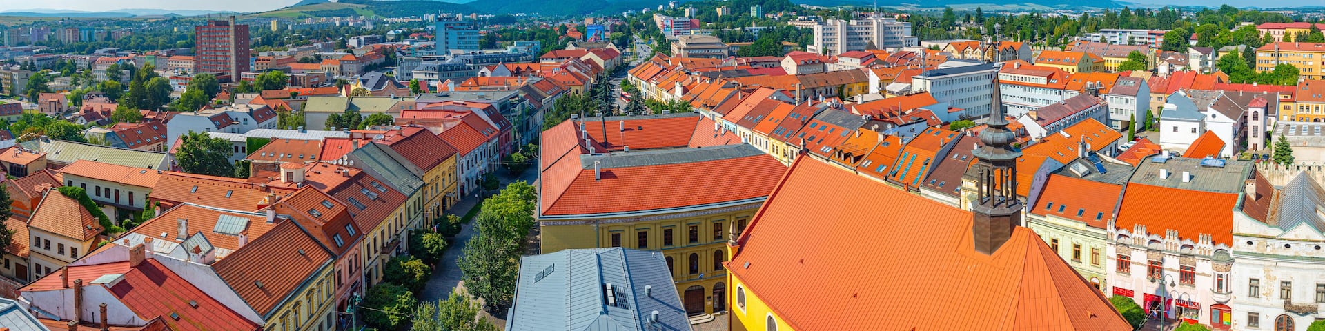A cityscape with red-roofed buildings, a prominent yellow building, and a distant mountain range.