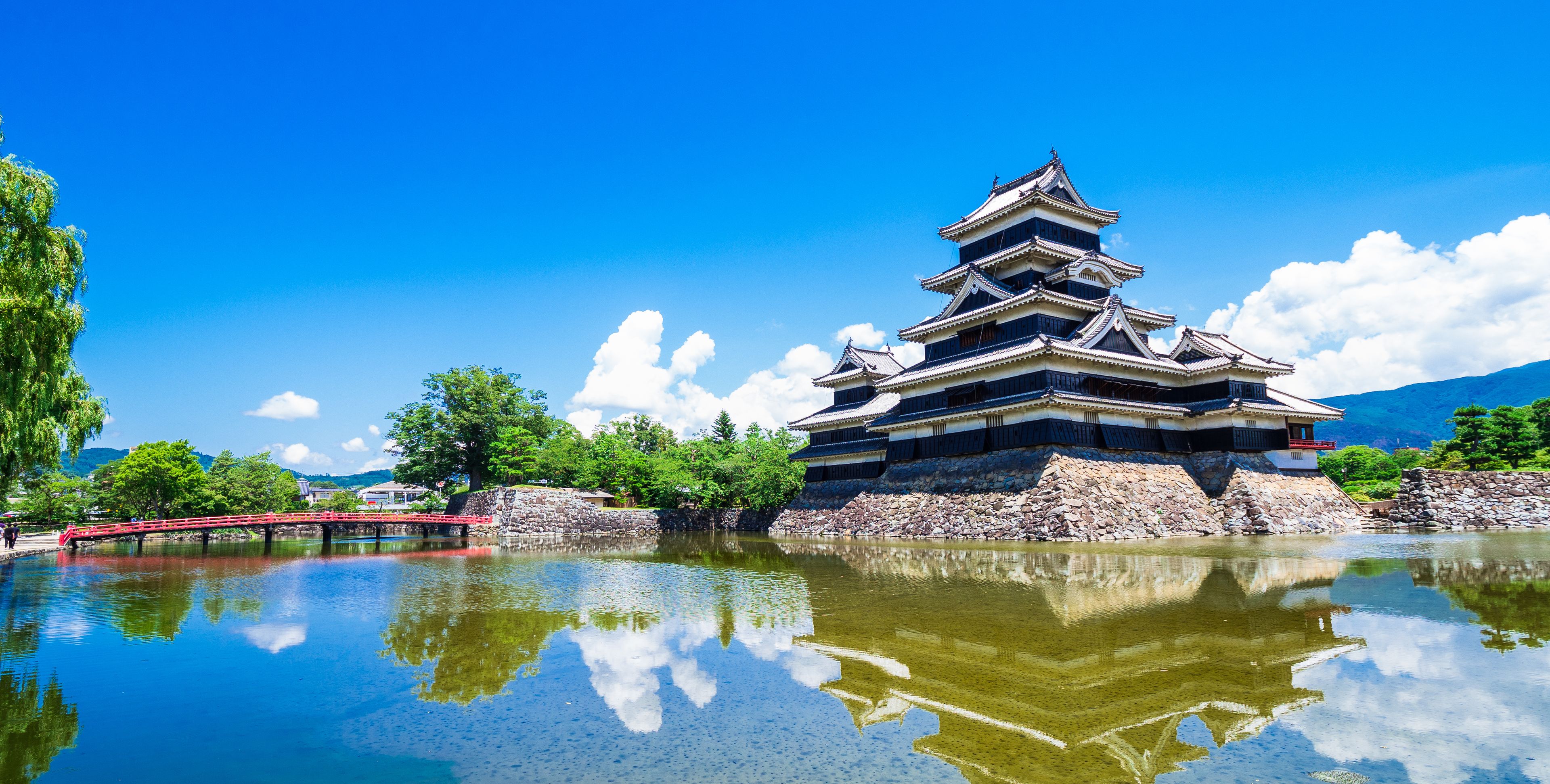 A traditional Japanese castle with multiple tiers, a stone base, and a reflection in the water.