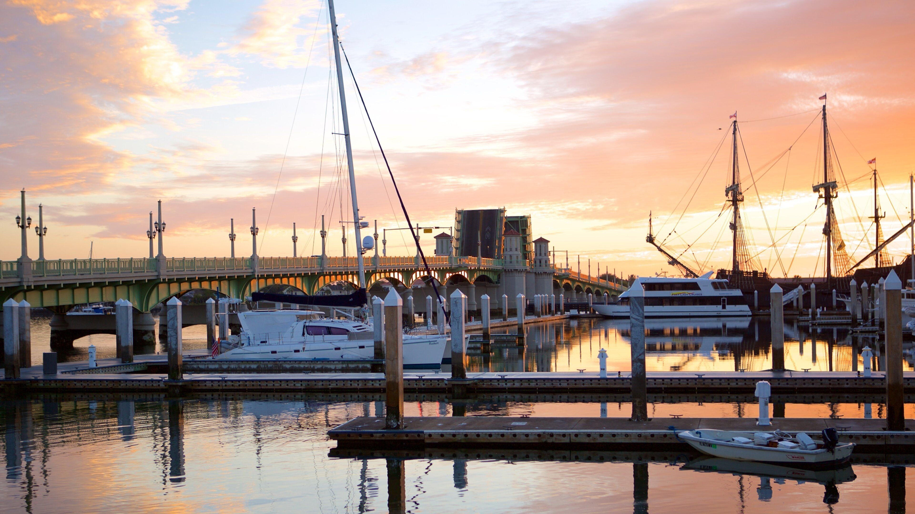 A marina with boats docked, a bridge, and a sunset sky.