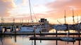 A marina with boats docked, a bridge, and a sunset sky.