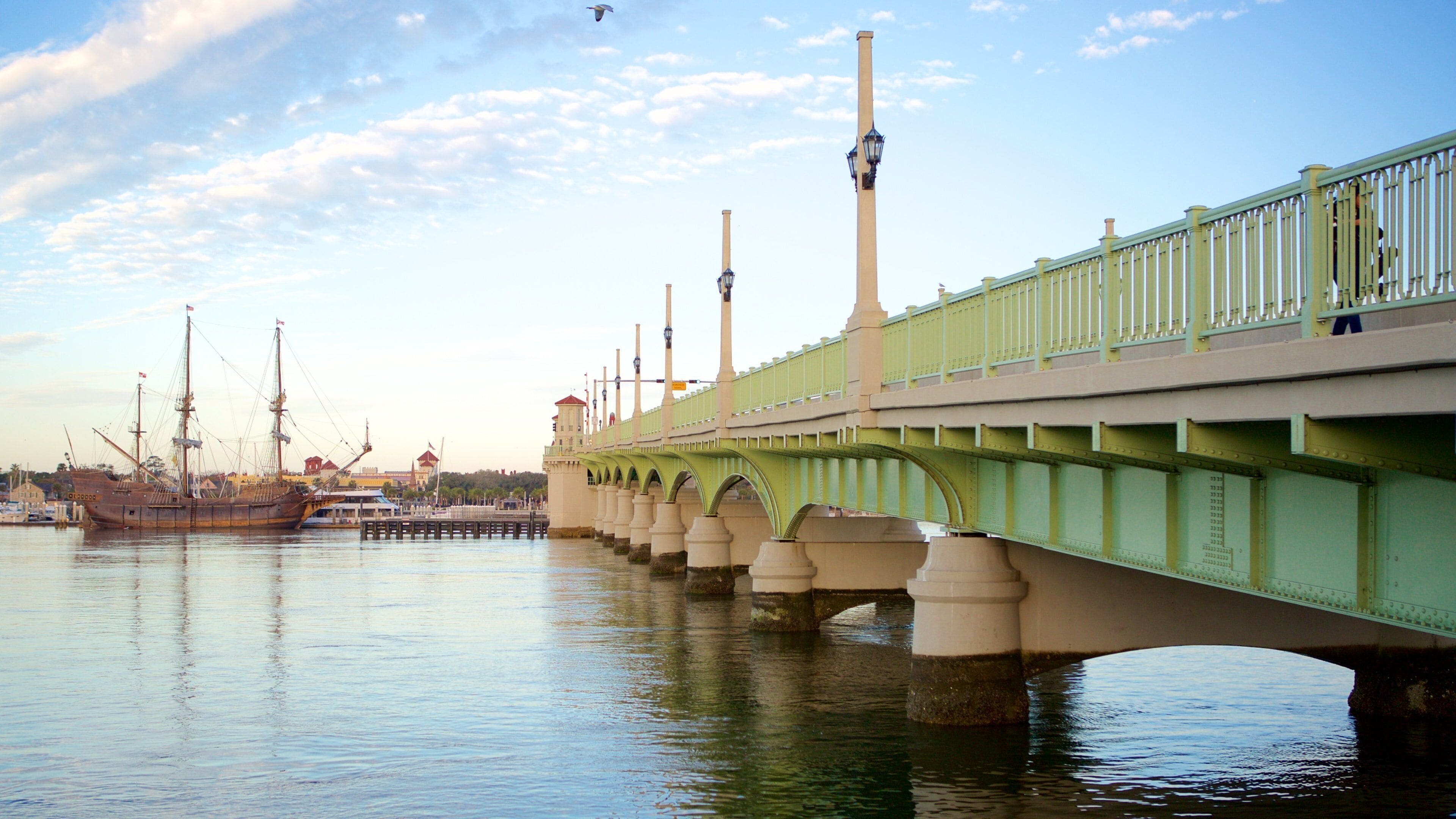 Eine grüne Brücke über Wasser, im Hintergrund Schiffe.