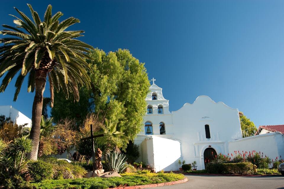 A white church with a bell tower, surrounded by palm trees and greenery.