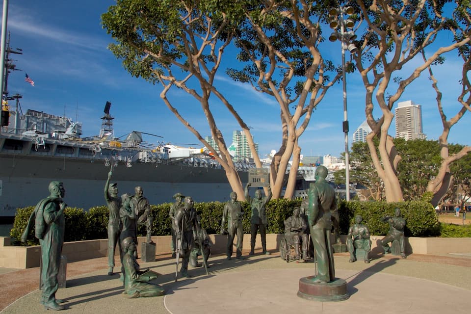 A naval ship docked at a port with a statue of soldiers in the foreground.
