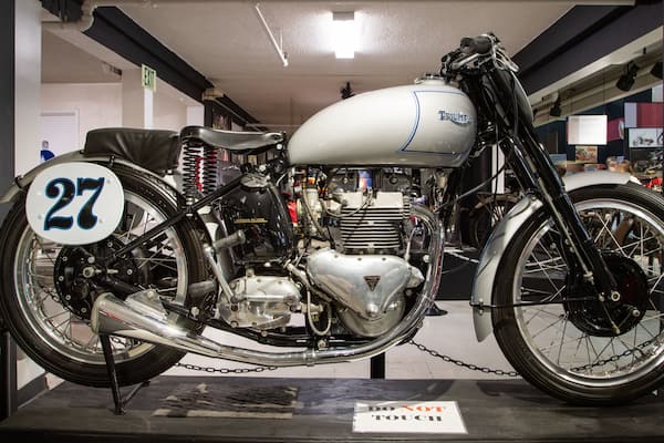 Ein restaurierter Triumph Motorrad im Ausstellungsstück, mit dem Nummernschild '27', chromfarbenem Motor und einem klassischen Design.