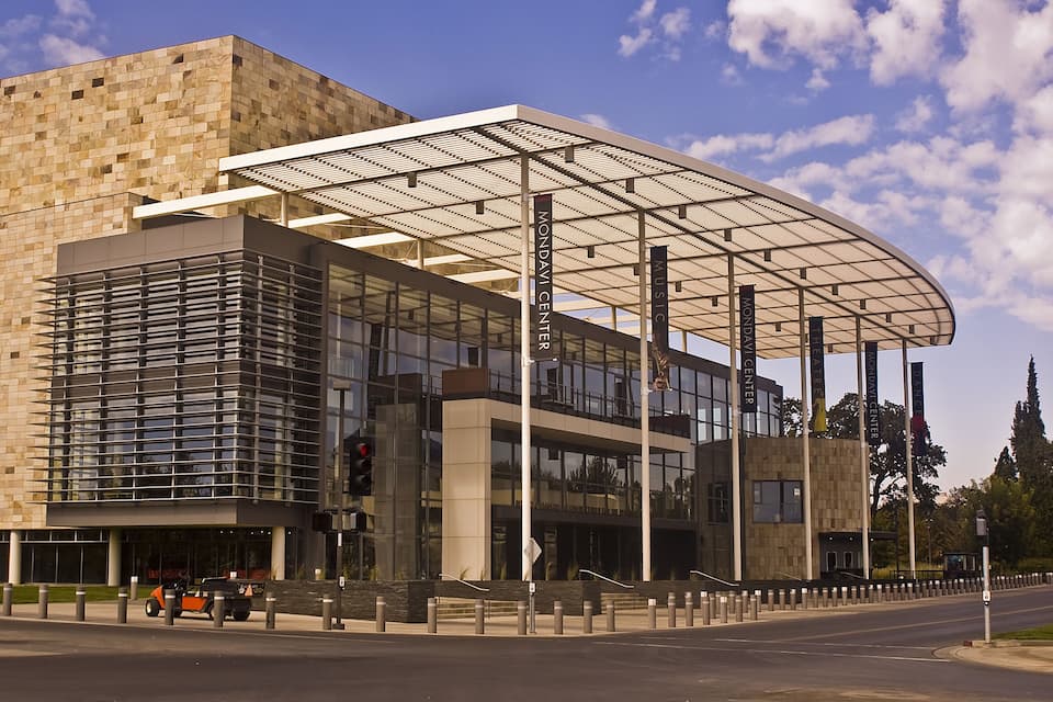 A modern building with a glass facade and a large overhanging roof structure.