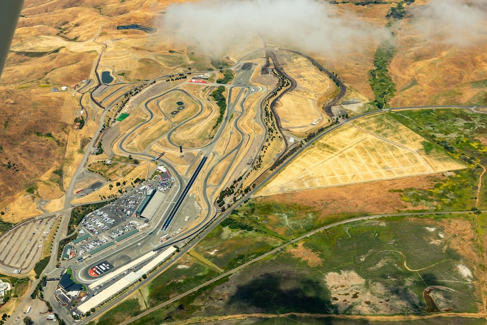 An aerial view of a complex highway interchange with multiple ramps and roads, surrounded by dry, hilly terrain and patches of greenery.