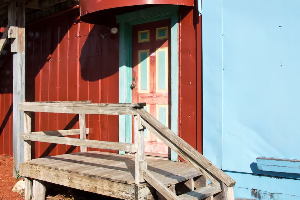 Une grange rouge avec une porte bleue et un escalier en bois menant à l’étage.