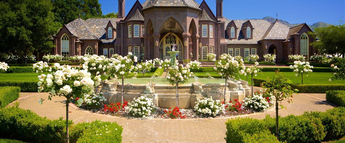 A large brick mansion with a central fountain surrounded by white and red flowers.