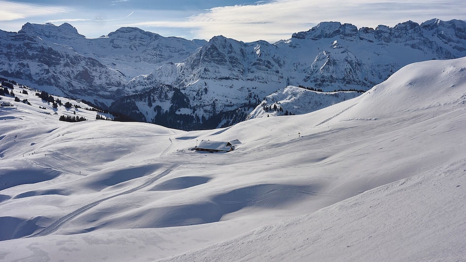 A snow-covered mountain landscape with a cabin in the distance and a clear sky.