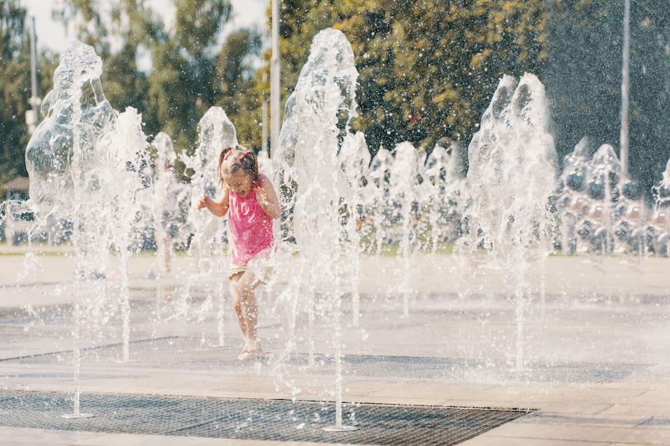A child playing in a water fountain area with multiple water jets.