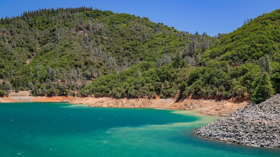 A turquoise coastal bay surrounded by forested hills.