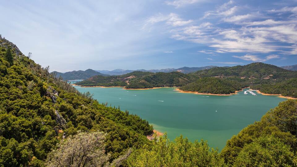 A coastal landscape with a bay, green hills, and a clear sky.