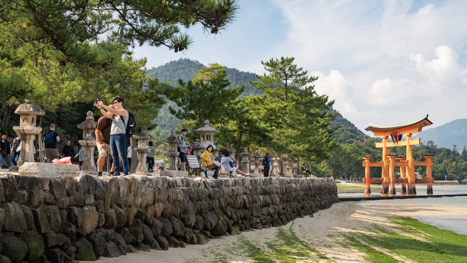 A stone wall with people taking photos, a traditional Japanese torii gate, and a mountainous backdrop.