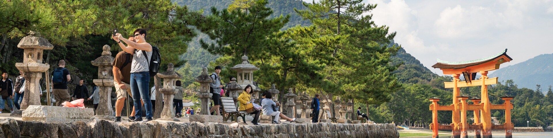 A stone wall with people taking photos, a traditional Japanese torii gate, and a mountainous backdrop.