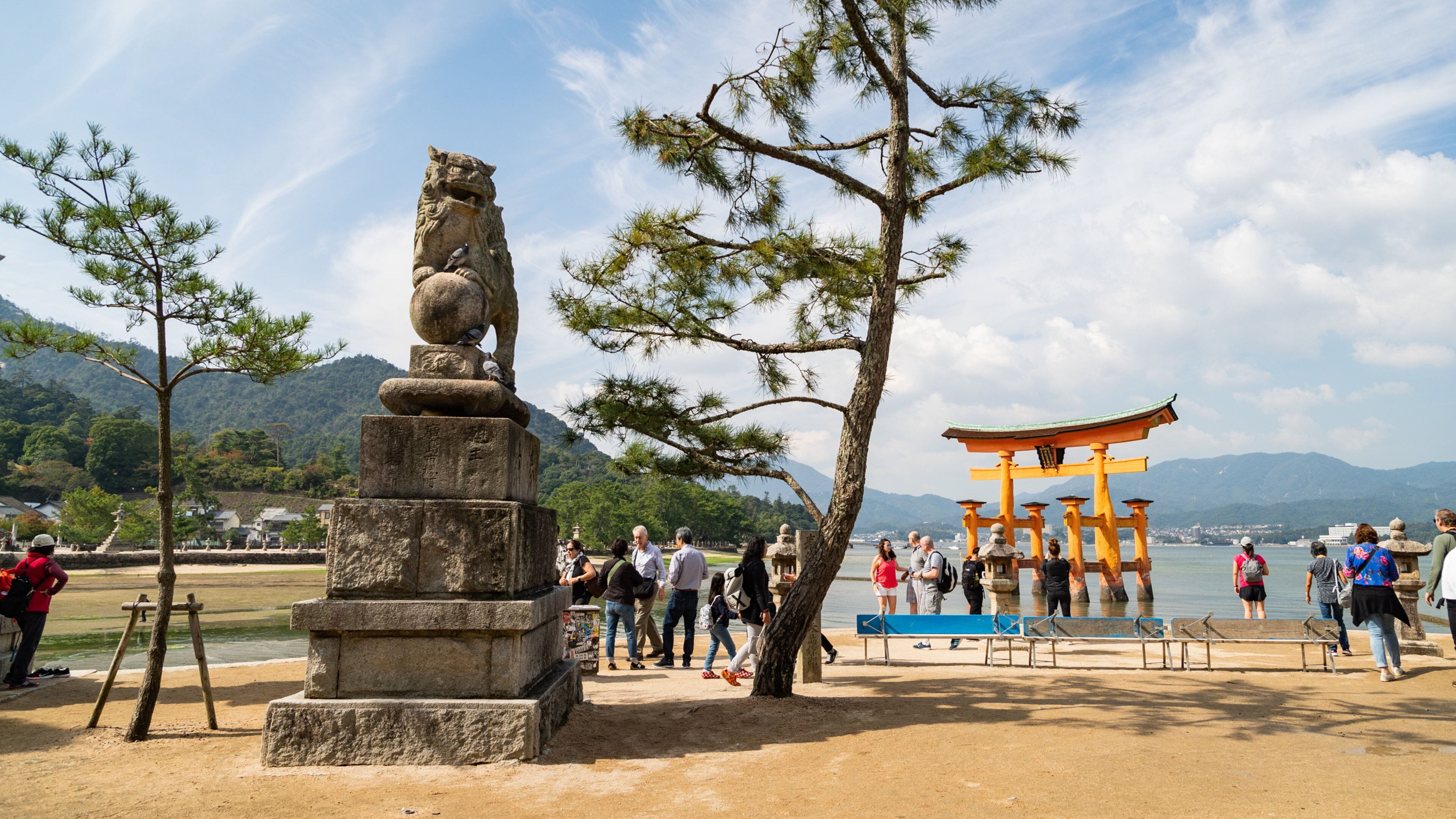 A stone lion statue, a traditional Japanese torii gate, and a lake with mountains in the background.