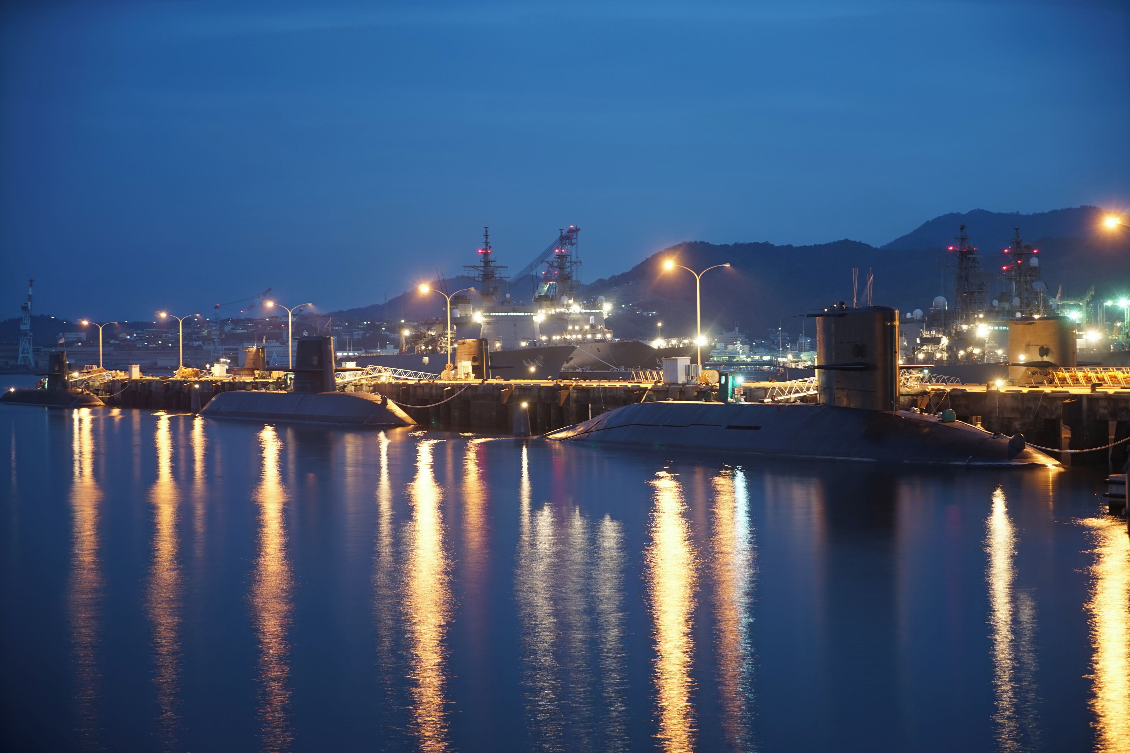 A nighttime harbor with illuminated ships and industrial structures reflecting on calm water.