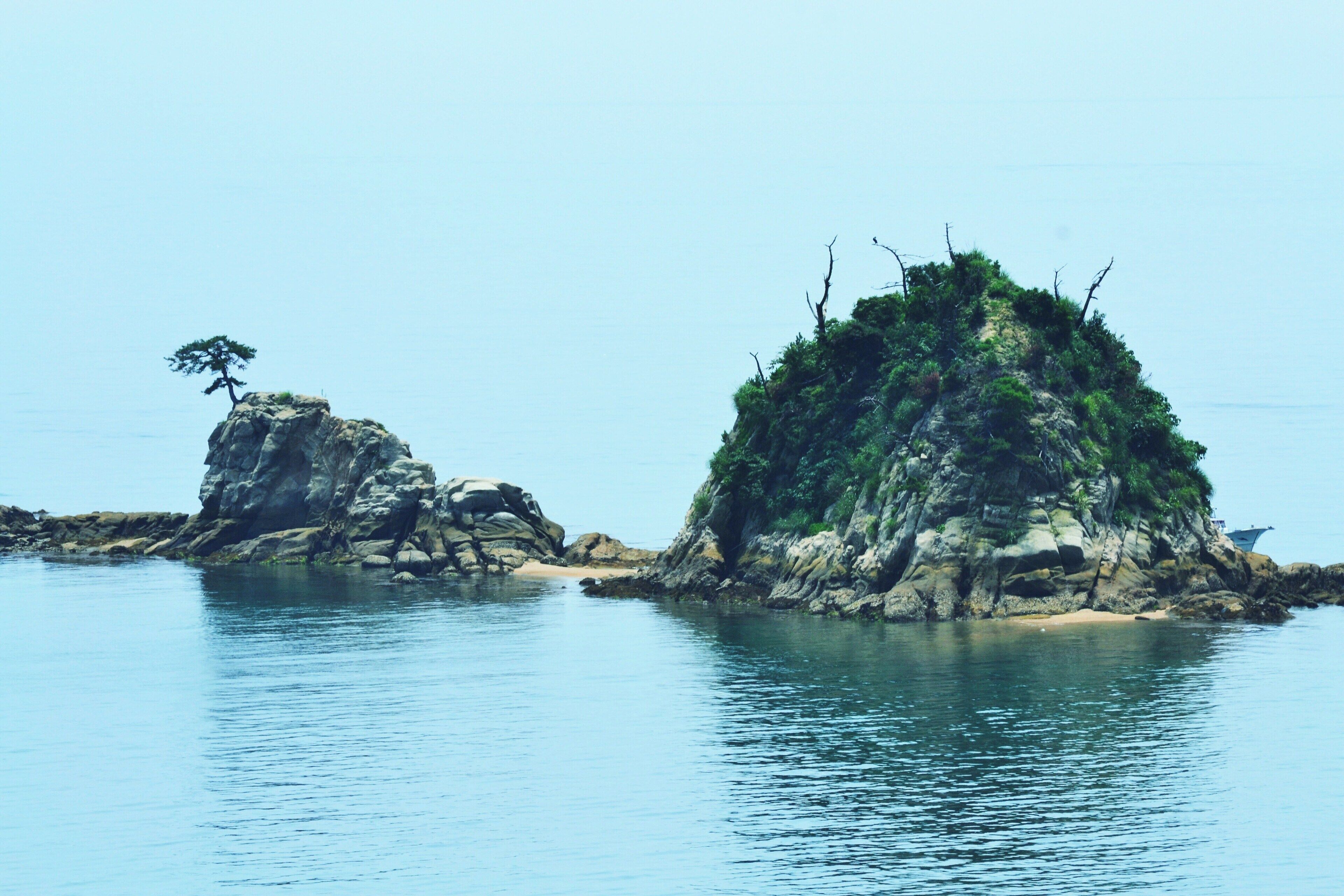 Mar tranquila con dos islas rocosas, una con un árbol solitario y la otra cubierta de vegetación.