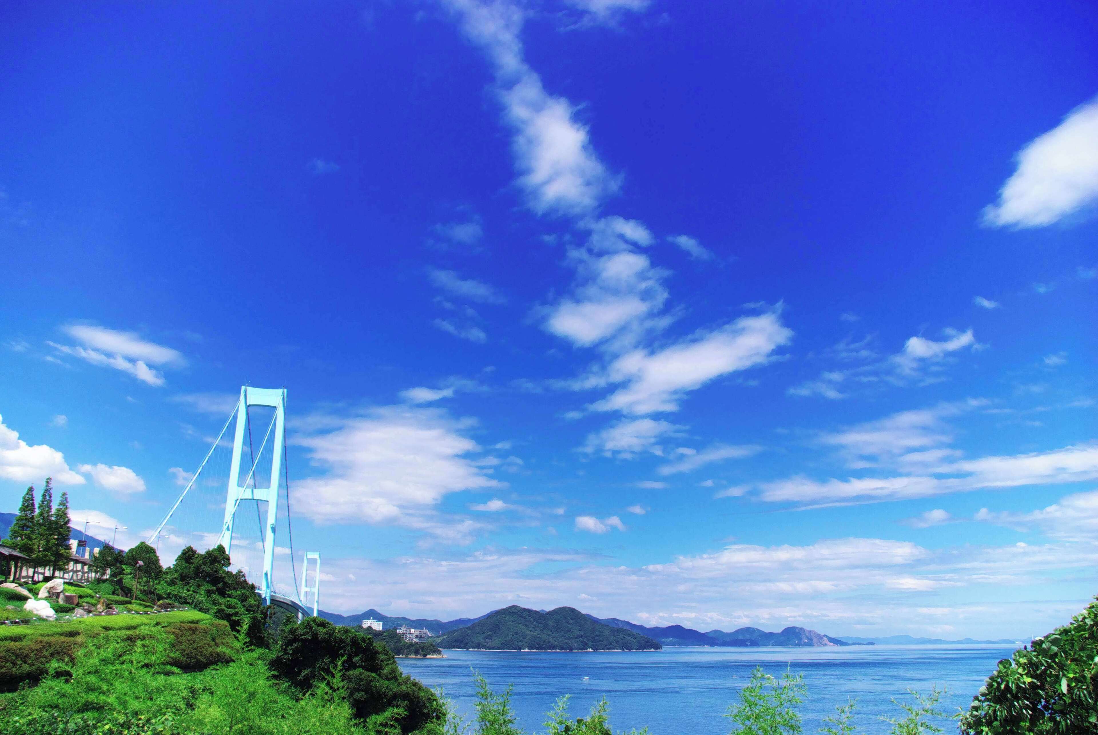 A suspension bridge, lush greenery, and a calm sea under a blue sky.