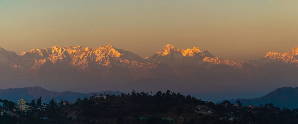 A mountain range with snow-capped peaks during sunrise or sunset.