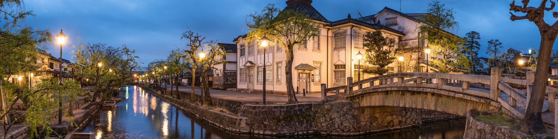 A canal with a wooden boat, stone bridge, and traditional buildings at dusk.