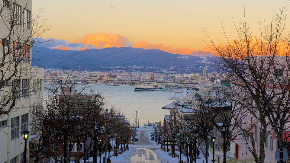 A cityscape with a river, mountains, and a sunset.